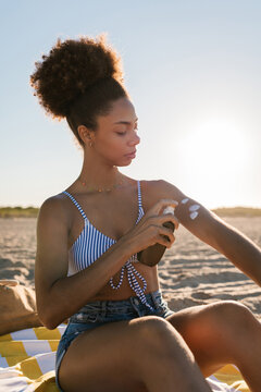 Young woman applying sunscreen to arm at beach