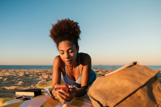 Young woman relaxing on beach using smartphone