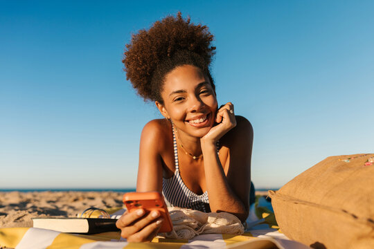 Smiling woman relaxing on beach looking at smartphone