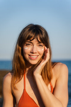Smiling woman applies sunscreen on her cheeks