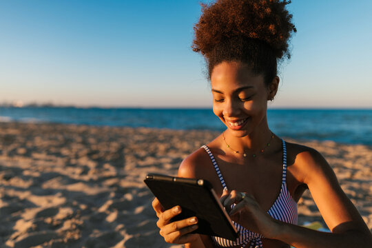 Young woman enjoying tablet on beach during vacation
