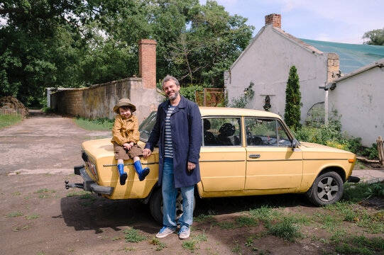 Father and son standing near a yellow car in a park