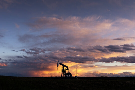 Oil Pump Jack Works at Sunset Under Clouds in the Field