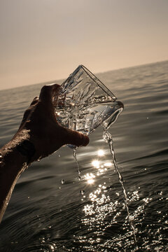 A hand holds a glass and fills it with seawater