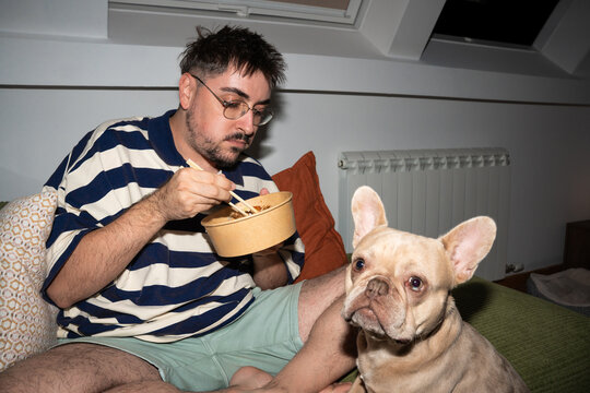 Man Eating Takeout Meal with French Bulldog at Home