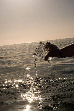 A hand holds a glass and fills it with seawater