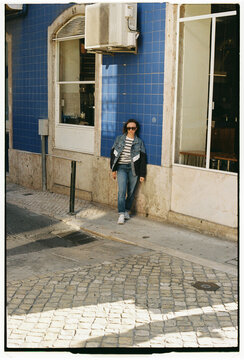 Woman Leaning Against Blue Tiled Building Facade in Lisbon Street