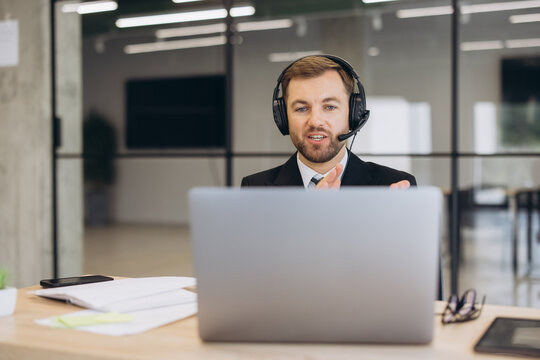 Businessman wearing headset communicating, providing online customer support during a video call on laptop in office