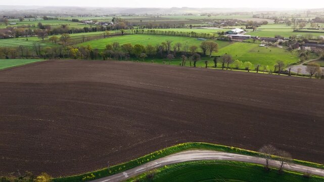 Farmland in Normandy, France, with green fields, brown plowed land and yellow flowering crop fields. Aerial agricultural view