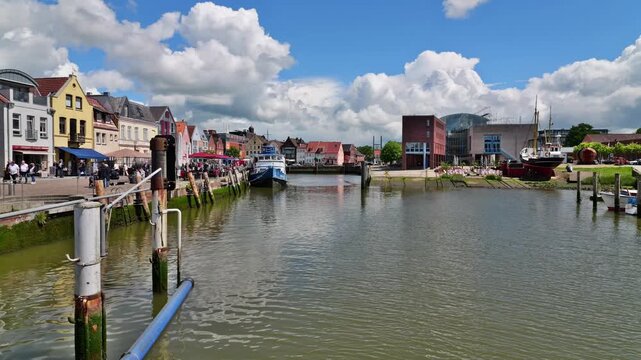 Harbor of Husum with the historic old town, waterfront promenade and dramatic clouds beneath a blue sky.