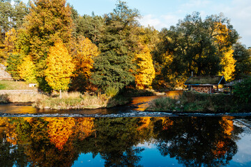 Autumn river forest with golden trees, rustic cabin and colorful reflections on calm water in sunny countryside © Mariana Verbenets