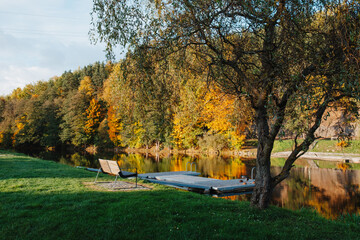 Empty bench and wooden dock by calm autumn river with golden forest reflections © Mariana Verbenets