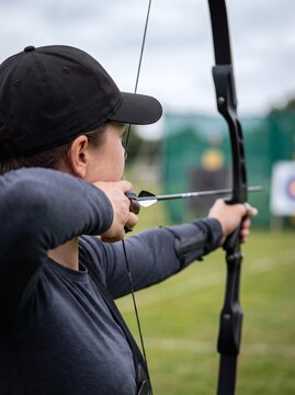 Woman aiming with a bow and arrow during an archery practice session outdoors, focusing on her target.