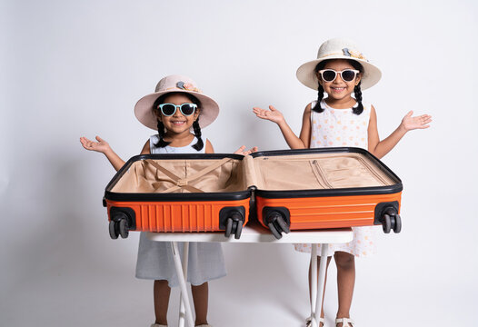 Two smiling indian girls posing with open empty orange suitcase white studio background summer vacation travel concept