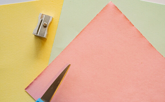 Papeler&iacute;a creativa con hojas de papel pastel, sacapuntas y l&aacute;piz sobre fondo colorido