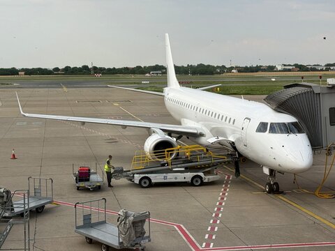All-white Embraer ERJ-190 without registration regional passenger jet airliner docked at airport terminal gate jetway during cargo baggage loading ground handling service operations. No brand or logo.
