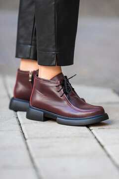 Burgundy leather oxford shoes with black cropped trousers standing on city sidewalk, polished urban fashion details, glossy finish, sharp contrast, modern street style