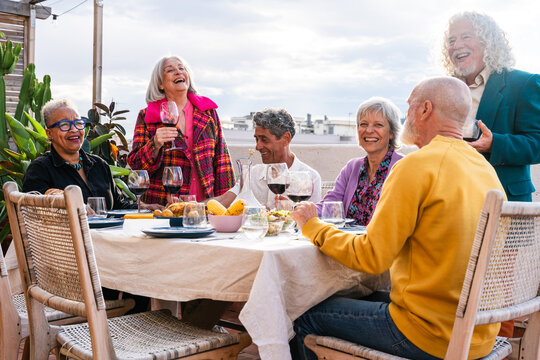Diverse senior friends enjoying dinner party on rooftop terrace