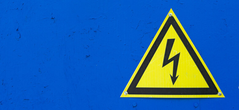 Yellow high voltage danger sign on blue background, chipped paint wall