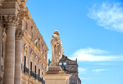 Set against a clear blue sky, the statue of Saint Peter stands majestically in front of the fa&ccedil;ade of Syracuse Cathedral