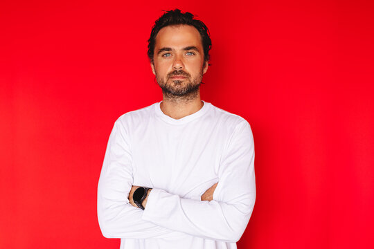 Serious confident middle aged Caucasian man standing with crossed arms looking at camera with calm neutral facial expression on bright red studio background portrait, leadership concept stock photo