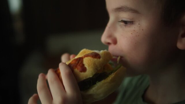 Close up of a child taking a bite of a homemade burger with fresh lettuce and a soft bun. Natural eating moment highlighting a tasty homemade meal and healthy appetite.