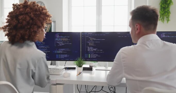 Programmers developers engineers practice teamwork coding. They collaborate at computer monitors in an office, reviewing software and planning tasks. Clear concept of collaborative coding teams.