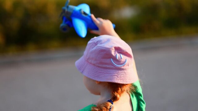 Child playing with a toy airplane outdoors. Small girl wearing a pink hat holding plastic aircraft above her head. Happy childhood, imagination, travel dream, and summer leisure activity.