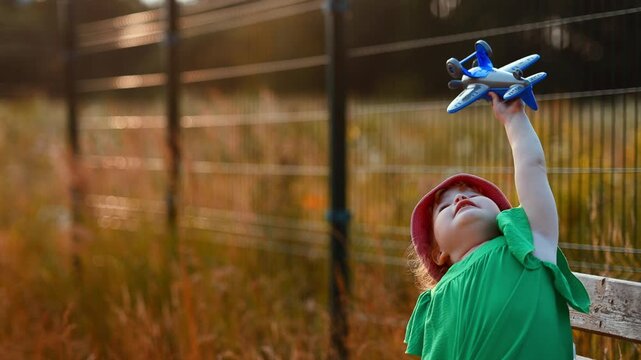 Child playing with a toy airplane outdoors. Small girl wearing a pink hat holding plastic aircraft above her head. Happy childhood, imagination, travel dream, and summer leisure activity.
