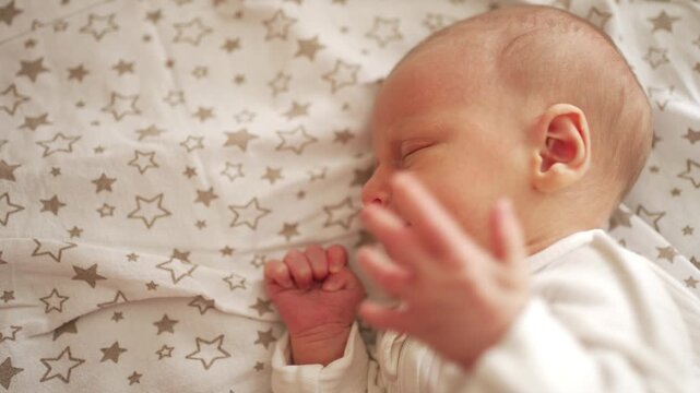 Close up top view of a newborn baby sleeping in a crib. Adorable infant rests on comfortable bedding with a star pattern, showing gentle breathing and small hand movements during sleep