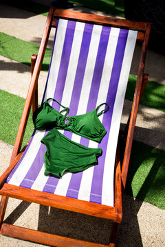 Green bikini set displayed on a purple and white striped lounge chair under sunlight, surrounded by green grass and outdoor elements