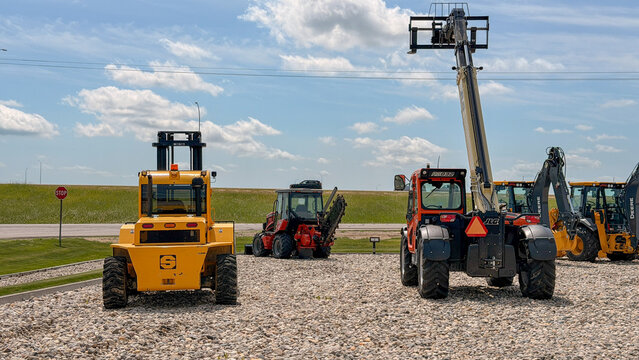 Regina, Canada - July 20, 2026: Multiple heavy construction machines including yellow forklift, JLC telehandler, and John Deere backhoe on gravel lot