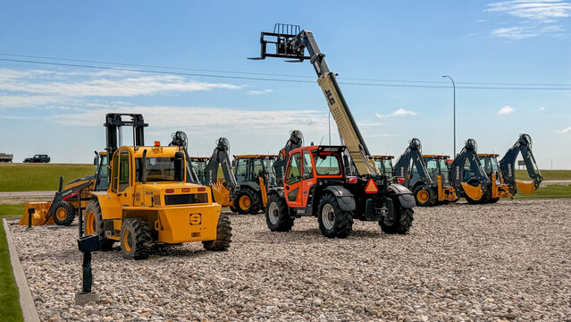Regina, Canada - July 20, 2026: Fleet of heavy construction equipment including John Deere backhoes, JLG telehandler, and yellow forklift parked on gravel lot