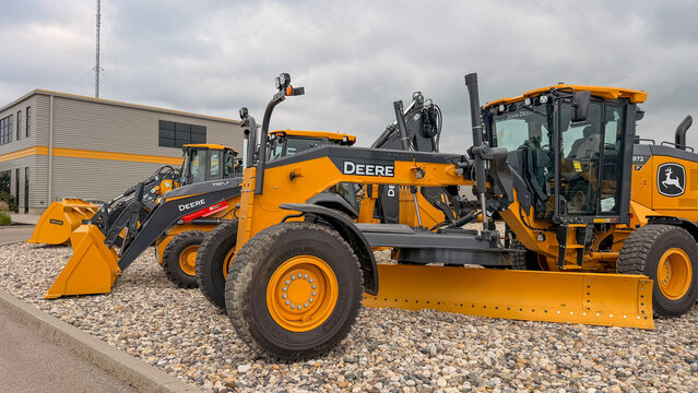 Regina, Canada - July 20, 2026: John Deere 872 motor grader and 710L backhoe loader parked on gravel lot outside dealership under overcast sky