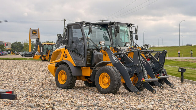 Regina, Canada - July 20, 2026: John Deere compact wheel loaders displayed on gravel lot at dealership with signage and backhoe visible in background