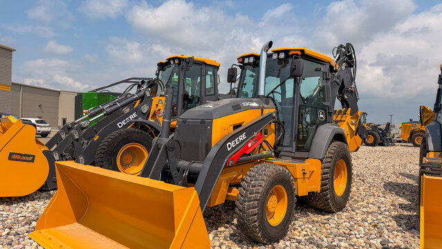 Regina, Canada - July 20, 2026: John Deere 320 backhoe loaders parked at Brandt dealership lot under summer sky