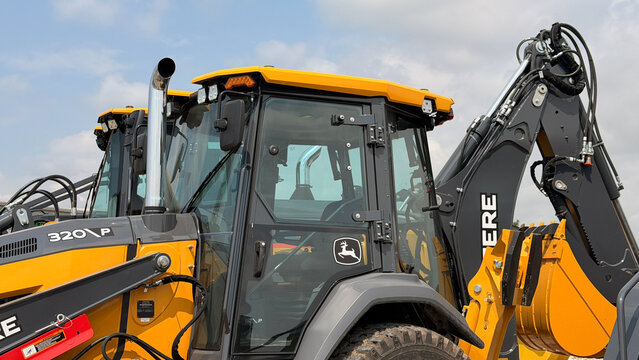 Regina, Canada - July 20, 2026: John Deere 320P backhoe loader cab close-up showing operator cabin, hydraulic arm, and yellow bodywork outdoors