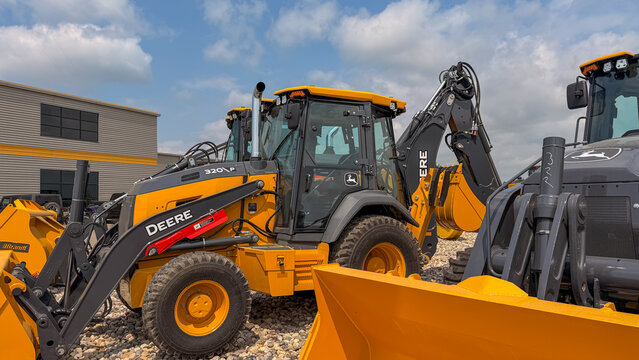 Regina, Canada - July 20, 2026: John Deere 320P backhoe loader parked at equipment dealership lot with blue sky background