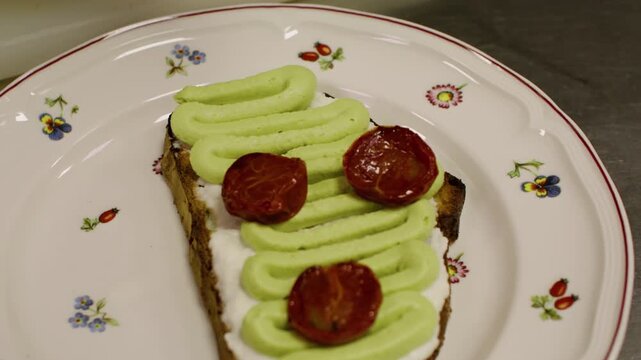 Cooking process. Making bruschetta. Chef plating tasty healthy meal with dried tomato. Gloved hand garnishing open sandwich with green cream.