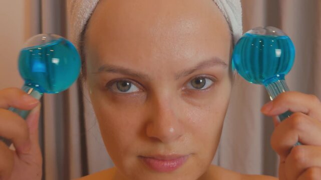 Young woman applying cryotherapy ice globes on her face, enjoying a refreshing and cooling facial massage to revitalize skin, reduce inflammation, and enhance her daily beauty and wellness routine