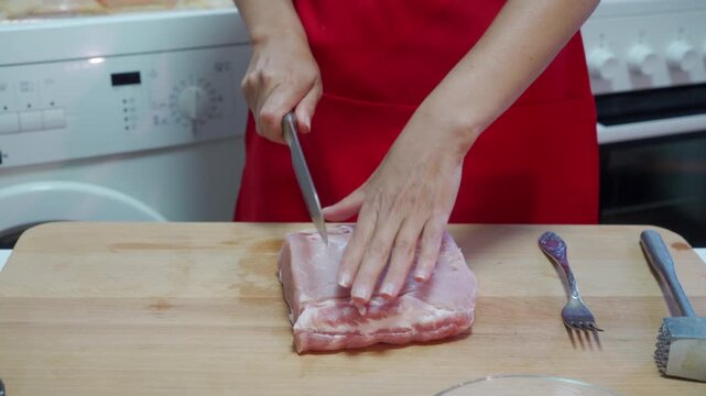 A focused woman carefully slices a block of raw meat on a wooden board in a tidy kitchen. She feels confident and determined as she prepares a hearty homemade dinner.