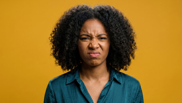 Young African American woman grimacing with a disgusted expression on a yellow background.