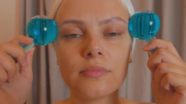 Woman applying cryosphere ice globes to her face, experiencing a refreshing and relaxing beauty treatment while reducing puffiness and promoting skin rejuvenation as part of her self care ritual