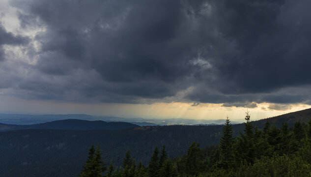 Dramatic god rays breaking through dark storm clouds over forested mountains of Krkonose National Park, Czech Republic
