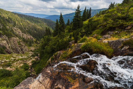 Elbe waterfall in Krkonose National Park, Czech Republic, flowing through a rocky mountain valley with green pine forests