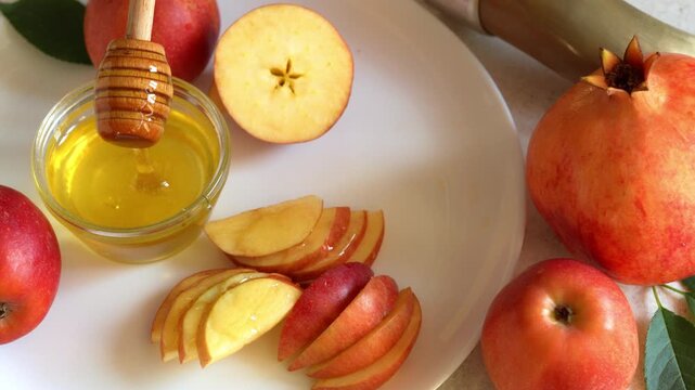 Happy Rosh Hashanah. Jewish New Year holiday concept. Honey dipper dripping honey to apples slices, next to apples, shofar horn and pomegranates.