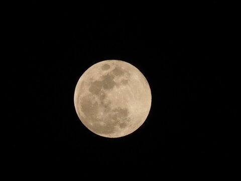 Full moon glowing warmly against a pitch black night sky, showing visible surface craters and detailed lunar geography.