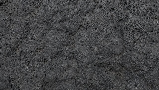 Close-up of dark porous volcanic rock texture with rough pitted surface and basaltic details