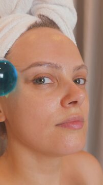 Woman applying blue cryosphere ice globes to her face, performing a refreshing facial massage for beauty, skincare, and reducing inflammation and puffiness