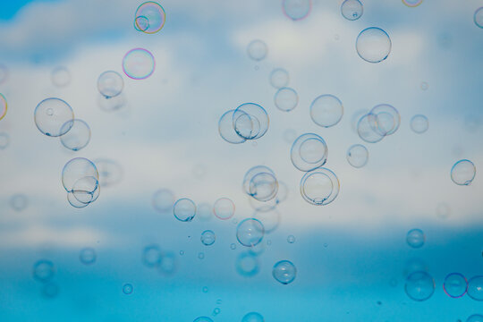 Transparent soap bubbles floating against a blue sky with soft clouds, creating a whimsical and light atmosphere in a natural outdoor setting